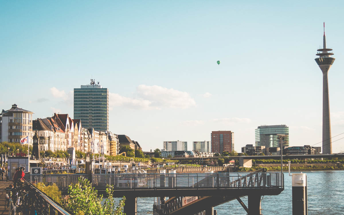 Strandpromenad längs floden Rhen i Dysseldorf i Tyskland. Solen skiner och reflekterar vackert på byggnaderna
